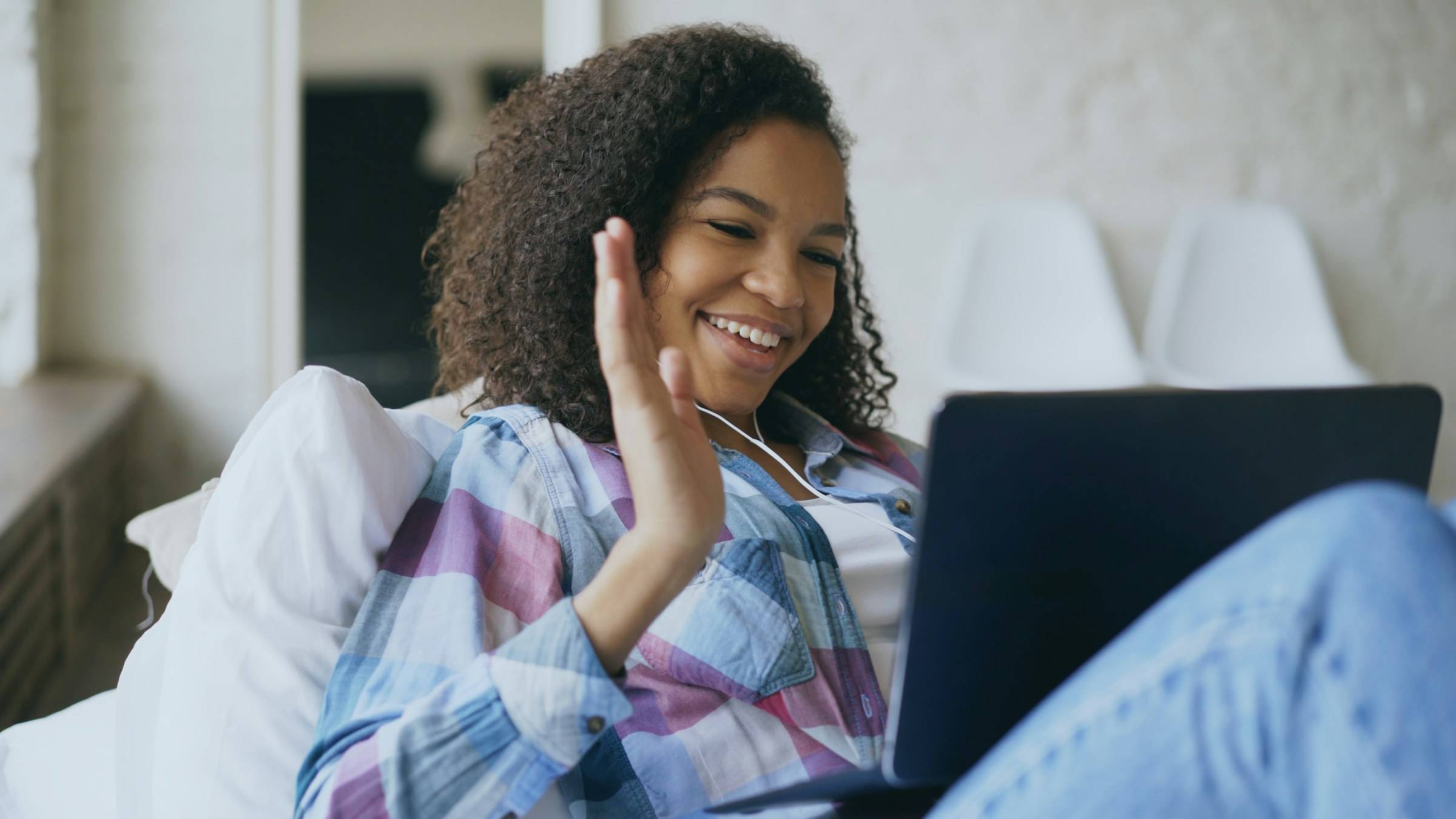 A young woman smiles and waves at her laptop during a video call